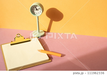 Clipboard and colored pencil, clock on pink desk. orange wall background. workspace Clipboard and colored pencil, clock on pink desk. orange wall background. workspace 111962336