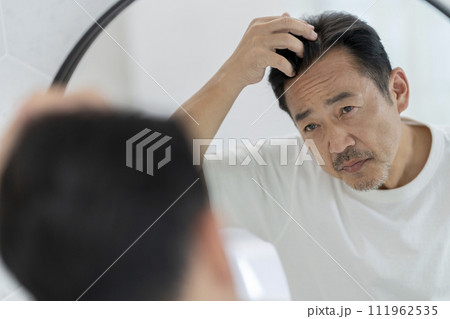 鏡を見ながら髪の生え際を気にする50代の男性 111962535