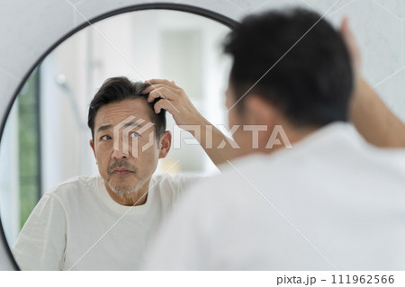 鏡を見ながら髪の生え際を気にする50代の男性 111962566
