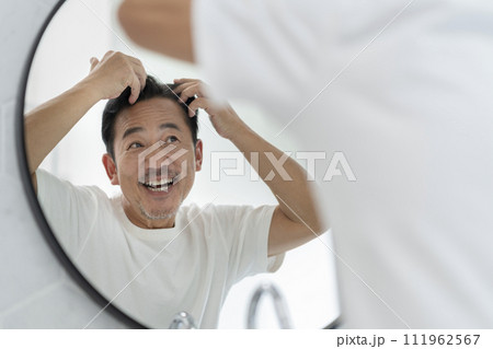 鏡を見ながら髪に触る笑顔の50代の男性 111962567