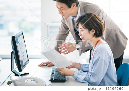 上司に相談しながらパソコン入力を行うビジネスパーソン 111962694