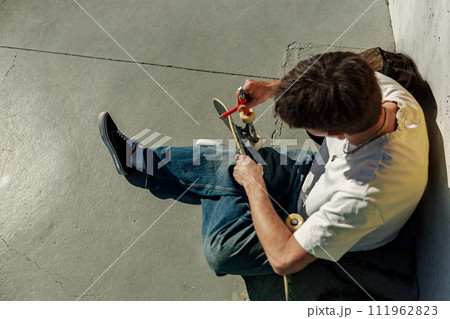 Stylish young man repairing his skateboard in the skate park. Extreme sport concept 111962823