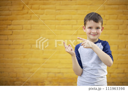 Smiling cute kid pointing with finger aside on yellow brick wall background Smiling cute kid pointing with finger aside on yellow brick wall background 111963398