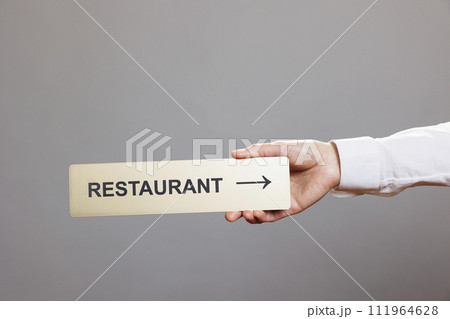 Woman hand holding restaurant directional stainless steel signage closeup. Receptionist arm showing cafeteria pointer tabletop metal sign close view in studio on gray background Woman hand holding restaurant directional stainless steel signage closeup. Receptionist arm showing cafeteria pointer tabletop metal sign close view in studio on gray background 111964628