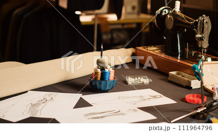 Modern clothes sketches on papers in tailor workshop, drawings used to create new fashion collection and clothing line with industrial tools or sewing machine. Small business atelier. Close up. 111964796