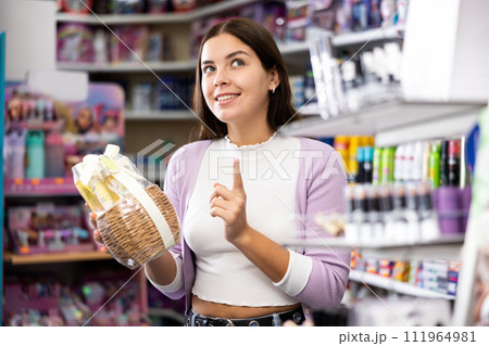 Positive young woman holding kit of haircare products in cosmetics shop 111964981