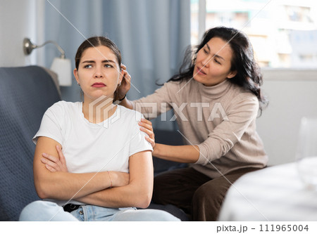 Woman comforting her friend after a domestic quarrel while sitting on couch 111965004
