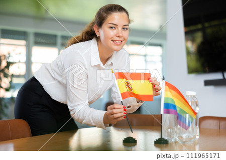 Young woman putting Spain and LGBT flags on table in office Young woman putting Spain and LGBT flags on table in office 111965171