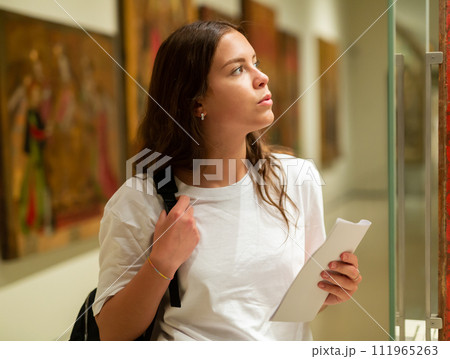 Girl visitor looks at the exhibit in the museum, located behind the glass 111965263