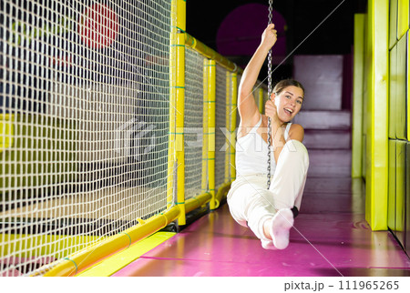 Cheerful young girl riding zip line in indoor amusement center 111965265