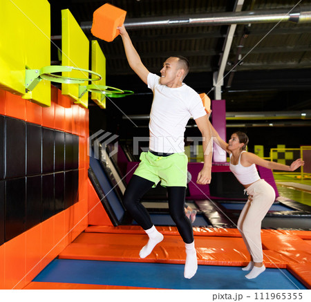 Athletic people throw ball into basketball basket while jumping on trampolines at an entertainment center Athletic people throw ball into basketball basket while jumping on trampolines at an entertainment center 111965355