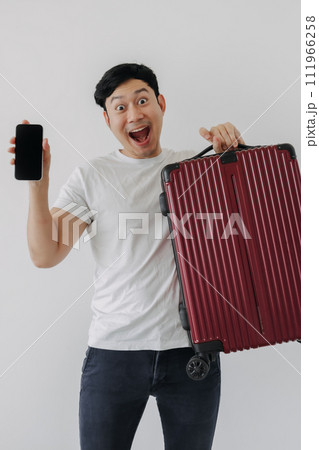 Asian man carrying a suitcase and holding mobile phone, showing application for travel and booking. Asian man carrying a suitcase and holding mobile phone, showing application for travel and booking. 111966258
