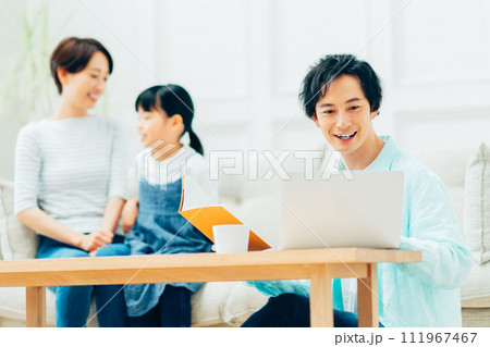 リビングでテレワークをするパパとくつろぐ家族。 リビングでテレワークをするパパとくつろぐ家族。 111967467