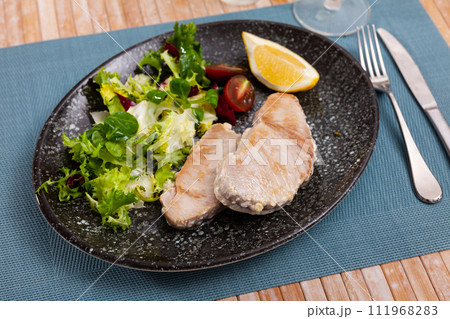 Prepared tuna steak served with lemon and tomato on plate on wooden table 111968283