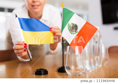 Woman secretary prepares an office for negotiations - she places flags of Ukrain and Mexico table 111968446