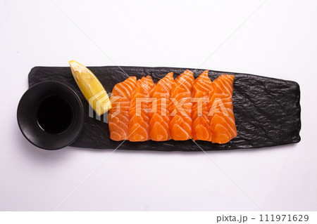 Freshly sliced salmon fillet isolated on a black stone plate with soy sauce and lemon wedge 111971629