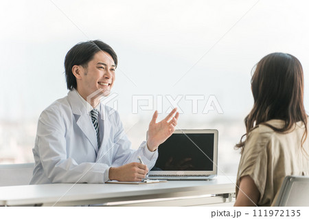 病院の診察室で問診・説明・診察する男性医師と受診する女性患者 病院の診察室で問診・説明・診察する男性医師と受診する女性患者 111972135