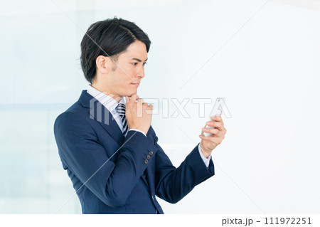 オフィスでスマホを見るアジア人男性ビジネスマン（考える・悩む・困る・思考・検討・想像） 111972251