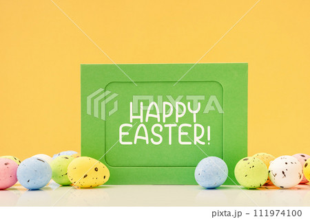 Happy Easter text on green mockup card with eggs and sweets on yellow. Copy space Happy Easter text on green mockup card with eggs and sweets on yellow. Copy space 111974100