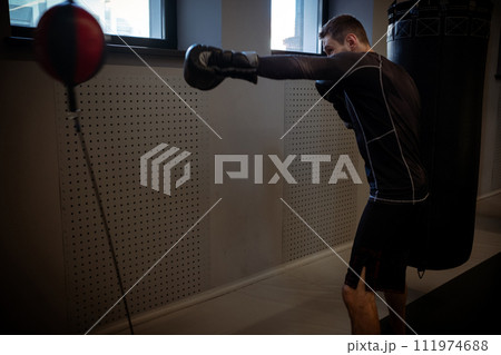 Intense workout of boxer practicing on floor-to-ceiling bag in gym 111974688