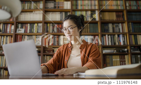 Concentrated female librarian working with books register on computer, keeping catalog 111976148