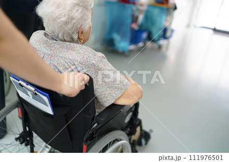 Close up of nurse pushing senior patient in wheelchair across hospital corridor. Emotional support for elderly woman. Close up of nurse pushing senior patient in wheelchair across hospital corridor. Emotional support for elderly woman. 111976501