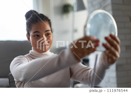 Portrait of beautiful curvy woman, looking at small round makeup mirror at home. 111976544