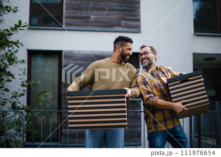 Man helping his friend move into new apartment in building. Man is moving into new flat, carrying box from the moving truck. Man helping his friend move into new apartment in building. Man is moving into new flat, carrying box from the moving truck. 111976654
