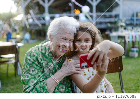 Young girl taking selfie with elderly grandmother at garden party. Love and closeness between grandparent and grandchild. 111976688