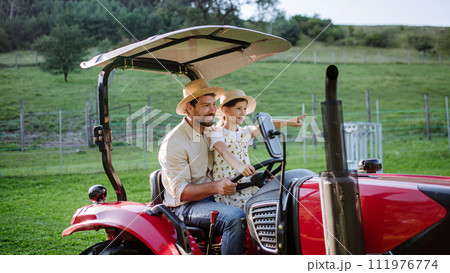 Farmer father riding tractor with his daughter. Girl growing up on family farm. Concept of multigenerational farming. Farmer father riding tractor with his daughter. Girl growing up on family farm. Concept of multigenerational farming. 111976774