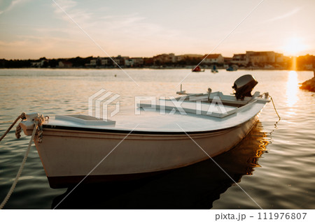 Small boat on calm water, moored in the harbor during sunset. Small boat on calm water, moored in the harbor during sunset. 111976807