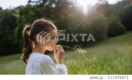 Portrait of beautiful young girl with blade of grass in mouth, standing on meadow, enjoying warm spring day. Portrait of beautiful young girl with blade of grass in mouth, standing on meadow, enjoying warm spring day. 111976871