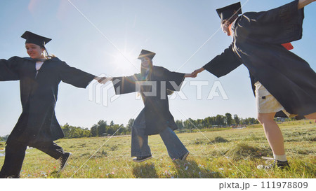College graduates holding hands run in a round dance. College graduates holding hands run in a round dance. 111978809