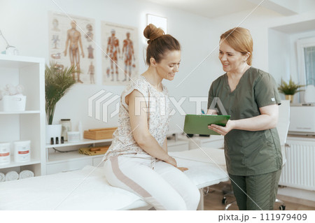 female therapist conducting examination and writing in clipboard 111979409