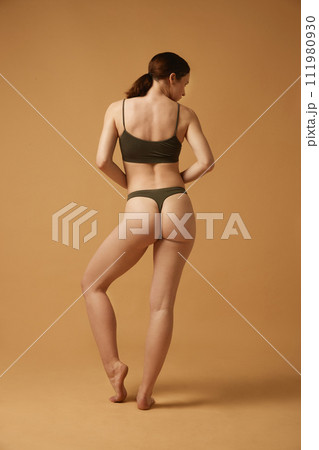 Full-length image of brunette young girl with slim, healthy, relief body, posing in cotton underwear against beige studio background 111980930