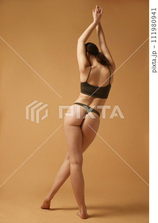 Well-being and body positive. Full-length image of slim, beautiful young woman with fit body standing in cotton underwear against beige studio background 111980941