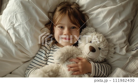 Child in striped pajamas lying in bed holding a teddy bear, looking happy and cozy. Child in striped pajamas lying in bed holding a teddy bear, looking happy and cozy. 111982430