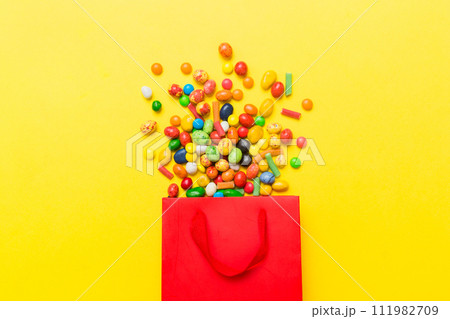 shopping paper gift bag in corner full of assorted traditional candies falling out on colored background with copy space. Happy Holidays sale concept 111982709