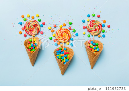 waffle cone full of assorted traditional candies falling out on colored background with copy space. Happy Holidays sale concept waffle cone full of assorted traditional candies falling out on colored background with copy space. Happy Holidays sale concept 111982728