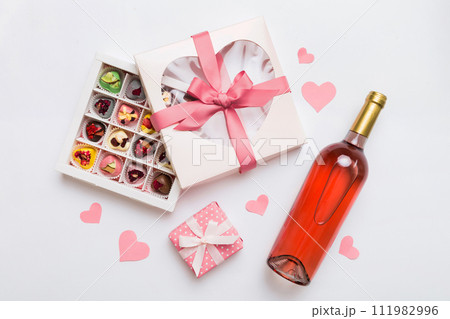 Bottle of red wine on colored background for Valentine Day with gift and chocolate. Heart shaped with gift box of chocolates top view with copy space 111982996