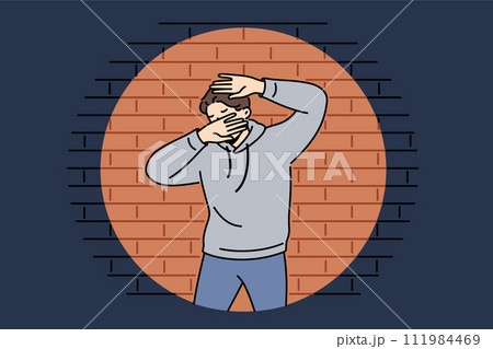 Man criminal in light of police lantern stands near brick wall and covers face with hands Man criminal in light of police lantern stands near brick wall and covers face with hands 111984469