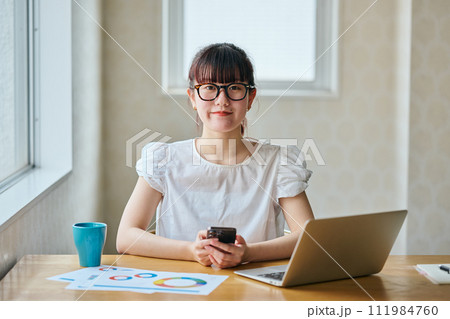 スマホを持ちテレワークをするカメラ目線の若い女性 スマホを持ちテレワークをするカメラ目線の若い女性 111984760