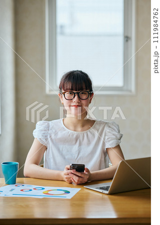 スマホを持ちテレワークをするカメラ目線の若い女性 111984762