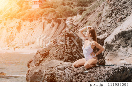 Woman travel sea. Happy tourist in white bikini enjoy taking picture outdoors for memories. Woman traveler posing on the beach at sea surrounded by volcanic mountains, sharing travel adventure journey 111985095