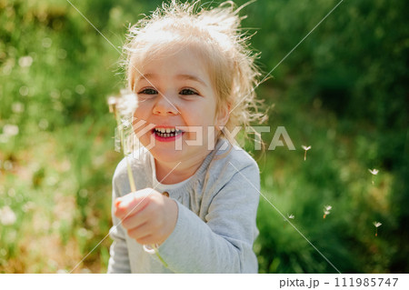 Cute little girl blow on a dandelion on spring sunny background 111985747