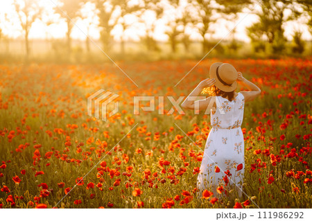 Beautiful girl in the poppy field at sunset in a white dress and hat. Beautiful girl in the poppy field at sunset in a white dress and hat. 111986292