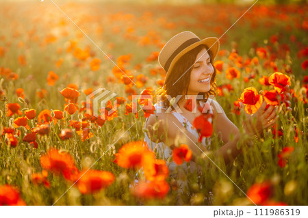 Beautiful girl in the poppy field at sunset in a white dress and hat. Beautiful girl in the poppy field at sunset in a white dress and hat. 111986319
