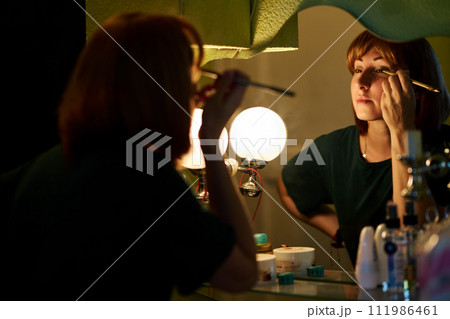 Beautiful young woman doing evening makeup Beautiful young woman doing evening makeup 111986461