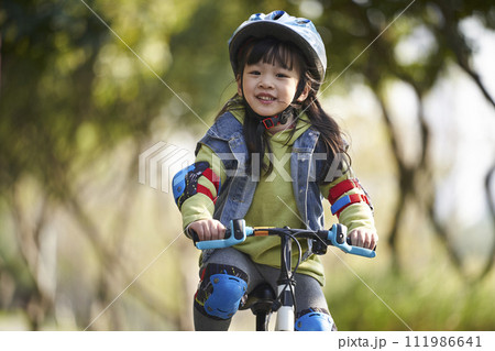 little asian girl riding bike outdoors in city park 111986641