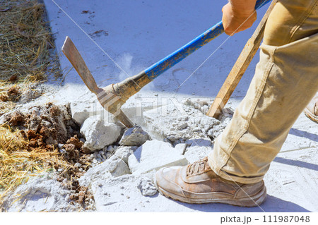 Worker smashes concrete old driveway with pickaxe on construction site Worker smashes concrete old driveway with pickaxe on construction site 111987048